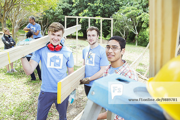 Porträt von lächelnden Freiwilligen mit Planken auf der Baustelle