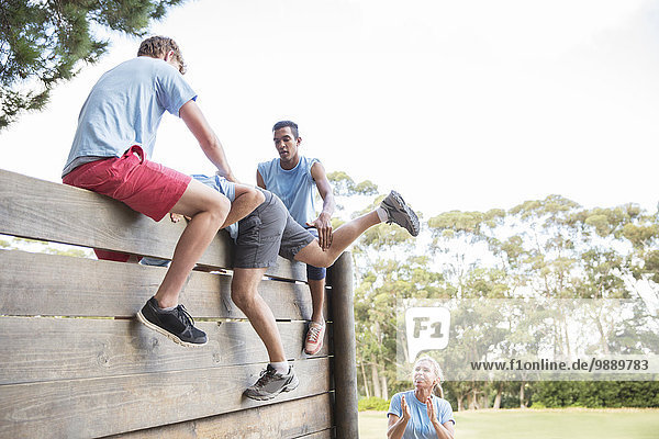 Teammates helping man over wall on boot camp obstacle course