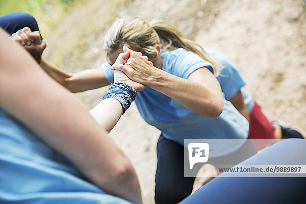 Mannschaftskameraden helfen der Frau beim Klettern im Bootcamp-Hindernisparcours