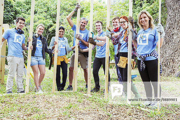 Portrait of smiling volunteers holding construction frame at construction site
