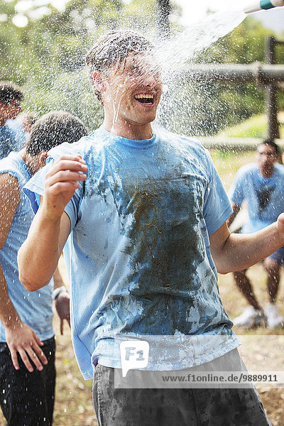 Enthusiastic man enjoying water hose spray on boot camp obstacle course