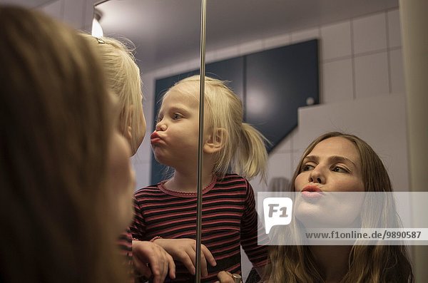 Über der Schulter Ansicht der weiblichen Kleinkind und Mutter puckering Lippen im Badezimmer Spiegel