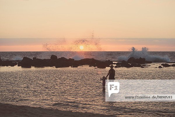 Silhouetted mother and female toddler paddling in sea looking out at waves splashing  Kona  Hawaii  USA