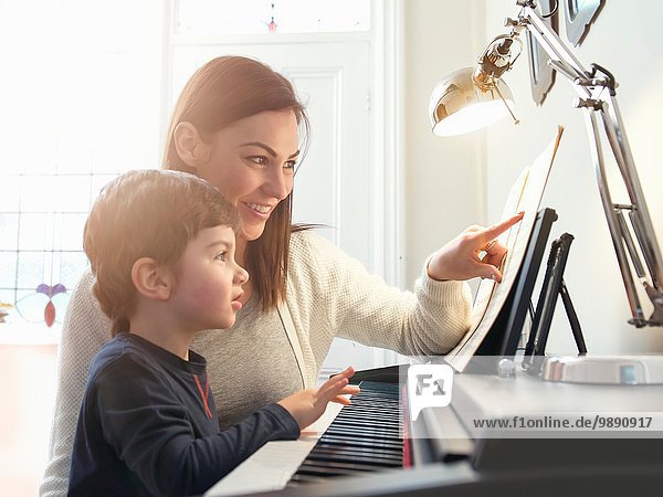 Mother pointing at sheet music to teach son to play piano at home