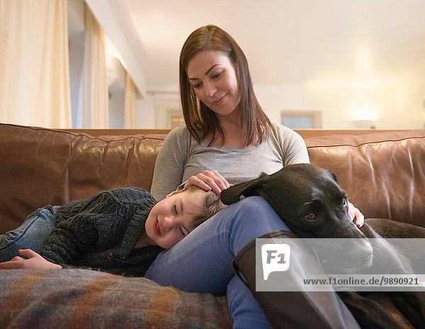 Mutter und müder Sohn entspannen auf dem Sofa zu Hause mit Haustier Labrador