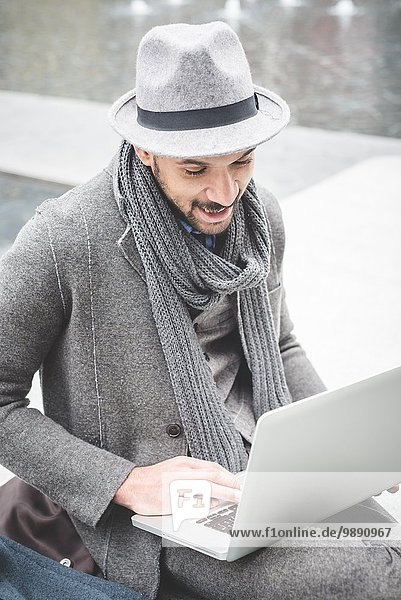 Smiling businessman sitting on wall using laptop