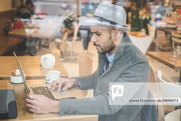 Businessman sitting in front of cafe window using laptop