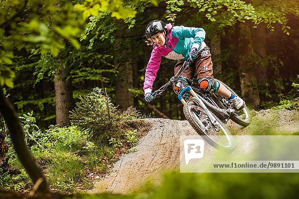 Young female mountain biker jumping on forest track