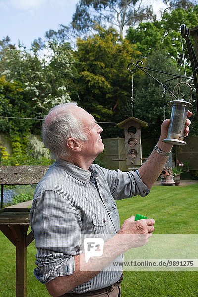 Senior Mann füllt Vogelfütterung im Garten nach
