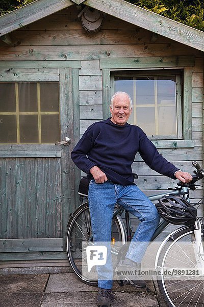 Älterer Mann  neben Schuppen mit Fahrrad stehend
