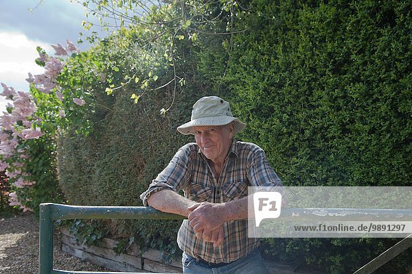 Älterer Mann  der sich auf den Gartenzaun stützt.