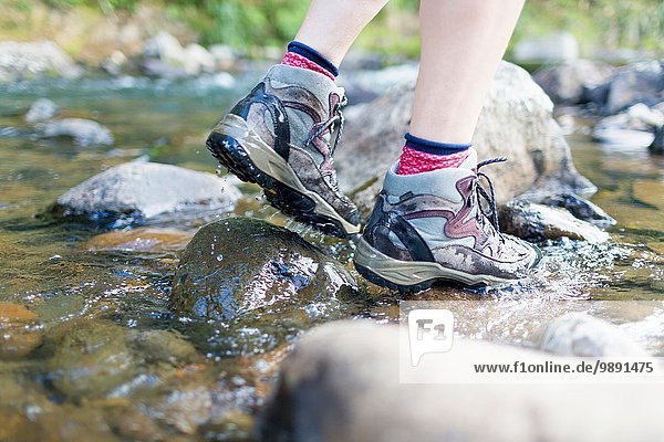 Hiker's feet walking on stones in shallow stream