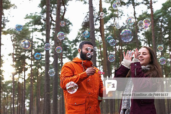 Young couple blowing bubbles in forest