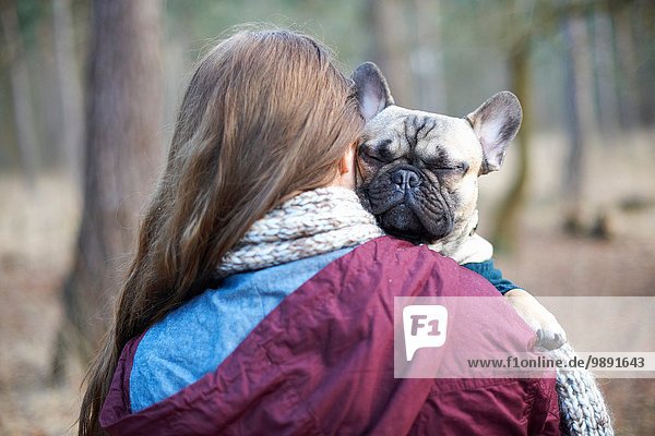 Portrait of cute dog being carried through forest by young woman