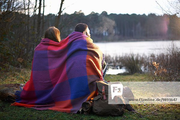 Young couple at lakeside wrapped in blanket at sunset
