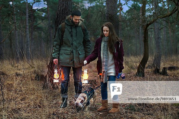 Young hiking couple with lanterns walking dog in woods