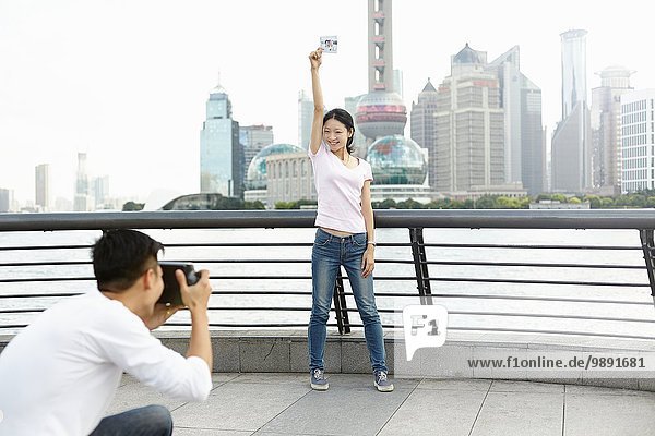Female tourist holding instant photo posing for boyfriend with instant camera  The Bund  Shanghai  China