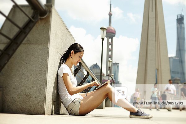 Junge Frau auf der Brücke sitzend mit Blick auf das digitale Tablett  The Bund  Shanghai  China