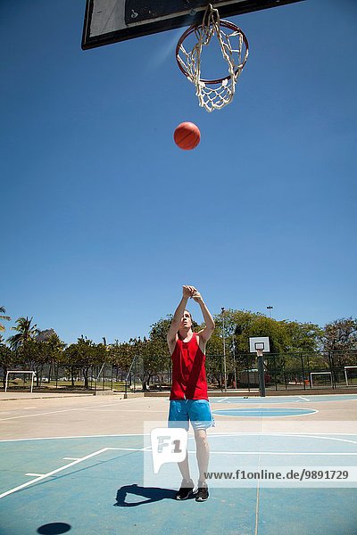 Junger Basketballspieler  der den Ball in Richtung Basketballkorb wirft.