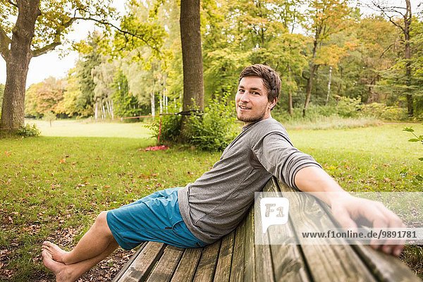 Portrait of barefoot young man sitting on park bench