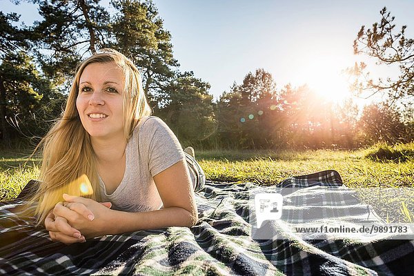 Porträt einer jungen Frau auf Picknickdecke im Park liegend