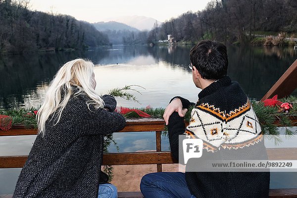 Heterosexuelles Paar auf Bank sitzend  am See  Blick auf die Lombardei  Italien