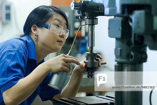Young woman using drill in industrial workshop