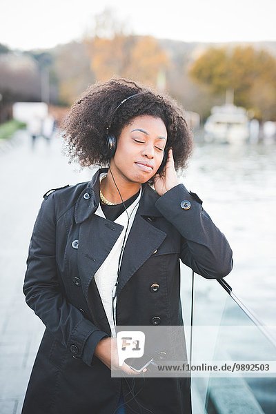 Young woman listening to headphones with eyes closed at Lake Como  Italy