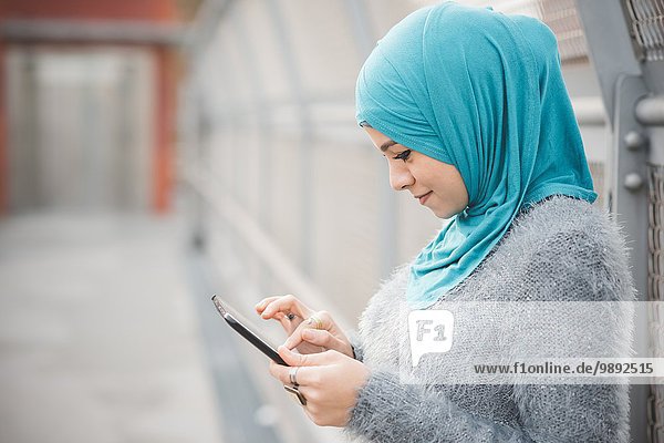 Junge Frau in türkisfarbenem Hijab mit digitalem Tablett auf Steg