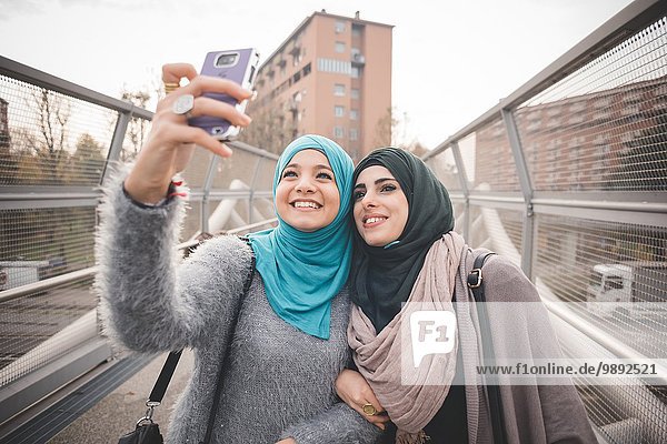 Two female friends on footbridge taking smartphone selfie