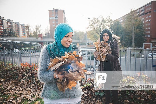 Two young women friends collecting autumn leaves in park
