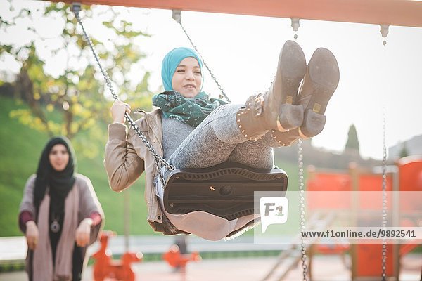 Two young women playing on playground swings