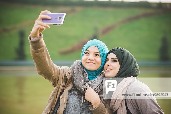 Zwei Freundinnen am Seeufer posieren für Smartphone Selfie