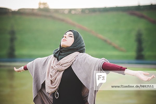 Young woman in park with arms open wearing hijab
