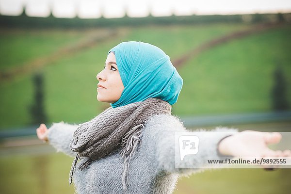 Junge Frau im Park mit offenen Armen in türkisfarbenem Hijab