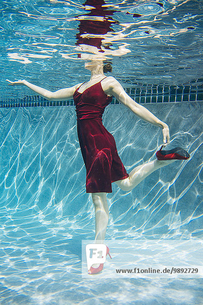 Mature woman wearing red dress and high heels  standing on one leg  underwater view
