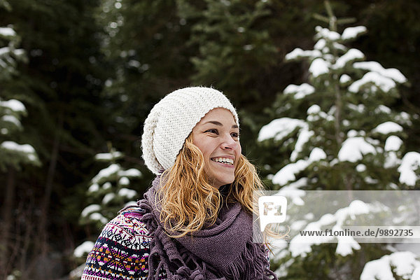 Porträt der lachenden jungen Frau vor schneebedeckten Tannenbäumen