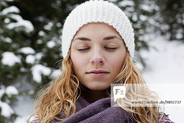 Nahaufnahme Porträt einer jungen Frau mit geschlossenen Augen vor schneebedeckten Tannenbäumen