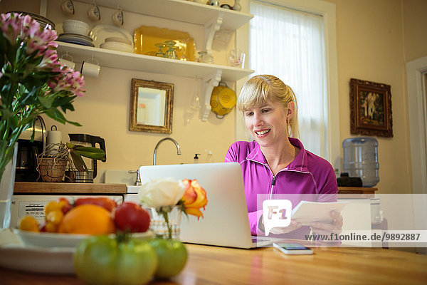 Frau arbeitet in der Küche Tisch Lesebuch und mit Laptop