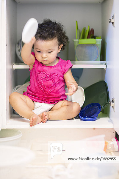Toddler girl sitting in kitchen cupboard