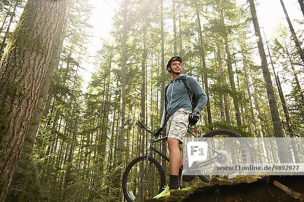 Young man standing with mountain bike in forest  low angle view