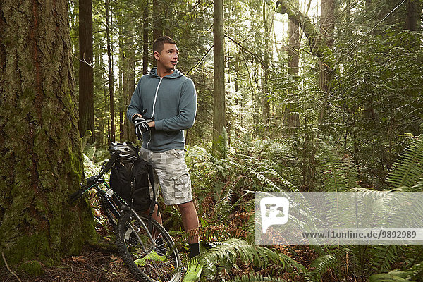 Young man in forest  leaning mountain bike against tree