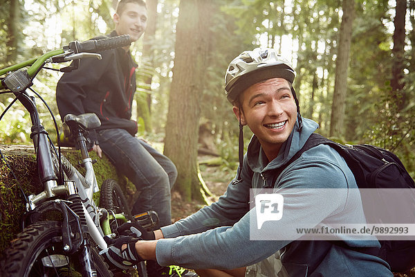 Young man fixing bike in forest while friend looks on