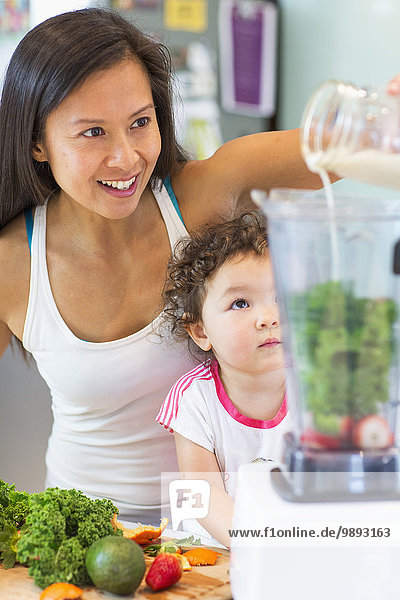 Mid adult woman making smoothie for toddler niece in kitchen