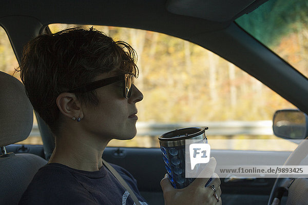 Mid adult woman drinking from flask whilst driving car