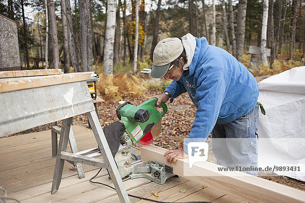 Älterer Mann sägt Brett aus Holz außerhalb des Hauses
