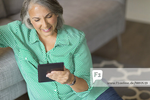 Mature woman sitting on floor next to sofa  using digital tablet