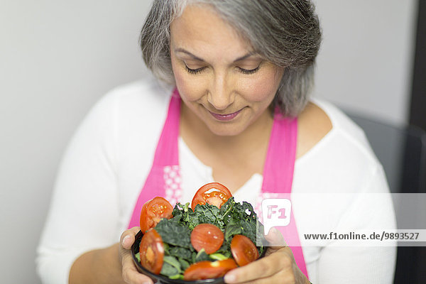 Reife Frau hält Schale mit Tomaten und Grünkohl