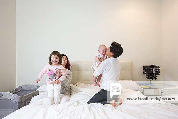 Female couple on bed playing with baby and toddler daughters