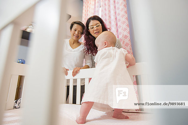 Female couple watching baby daughter in crib